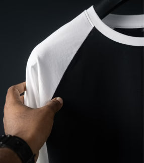 Black and white baseball shirt held by a hand against a dark background