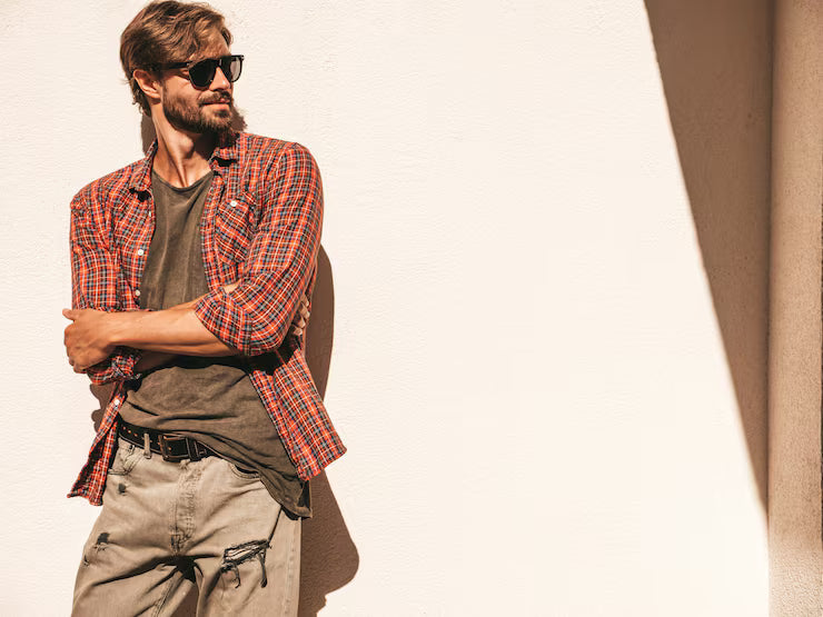 Man wearing a plaid shirt and sunglasses against a beige wall