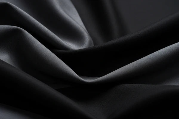 Close-up of draped black fabric with soft folds and a smooth, slightly glossy texture.
