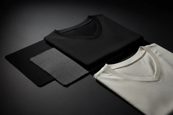 Two folded V-neck T-shirts, one black and one off-white, displayed on a dark reflective surface with two fabric texture swatches behind them.