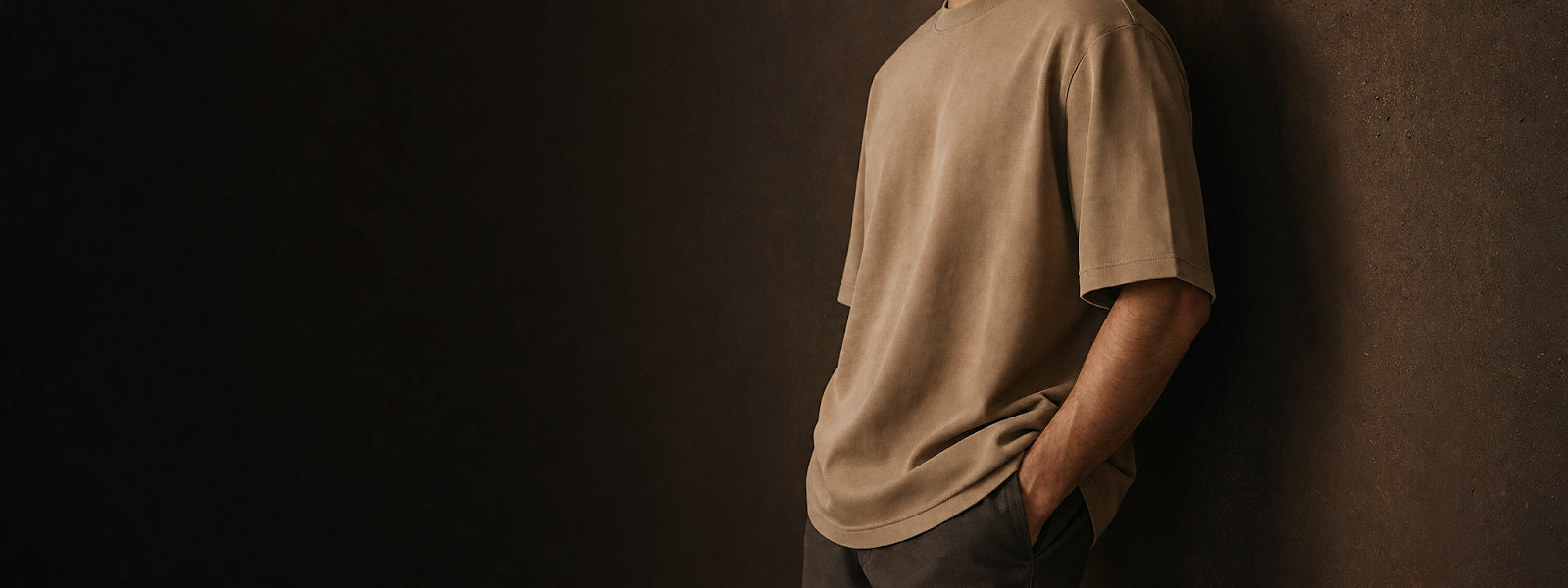 Person wearing a beige t-shirt against a dark wall